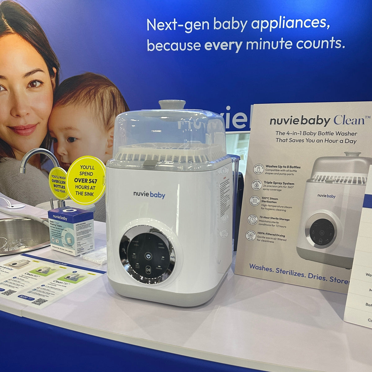 A nuviebaby Clean machine on a table in front of the expo backdrop, with a product information sign beside it