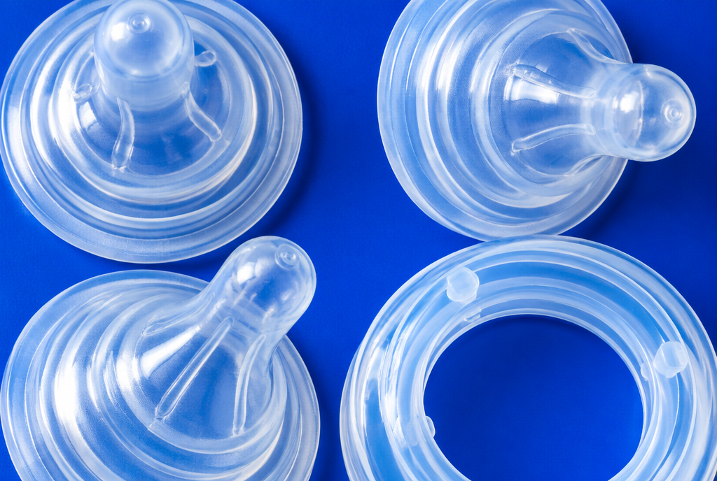 Three silicone baby bottle teats and a clear collar arranged on a cobalt blue surface, seen from above