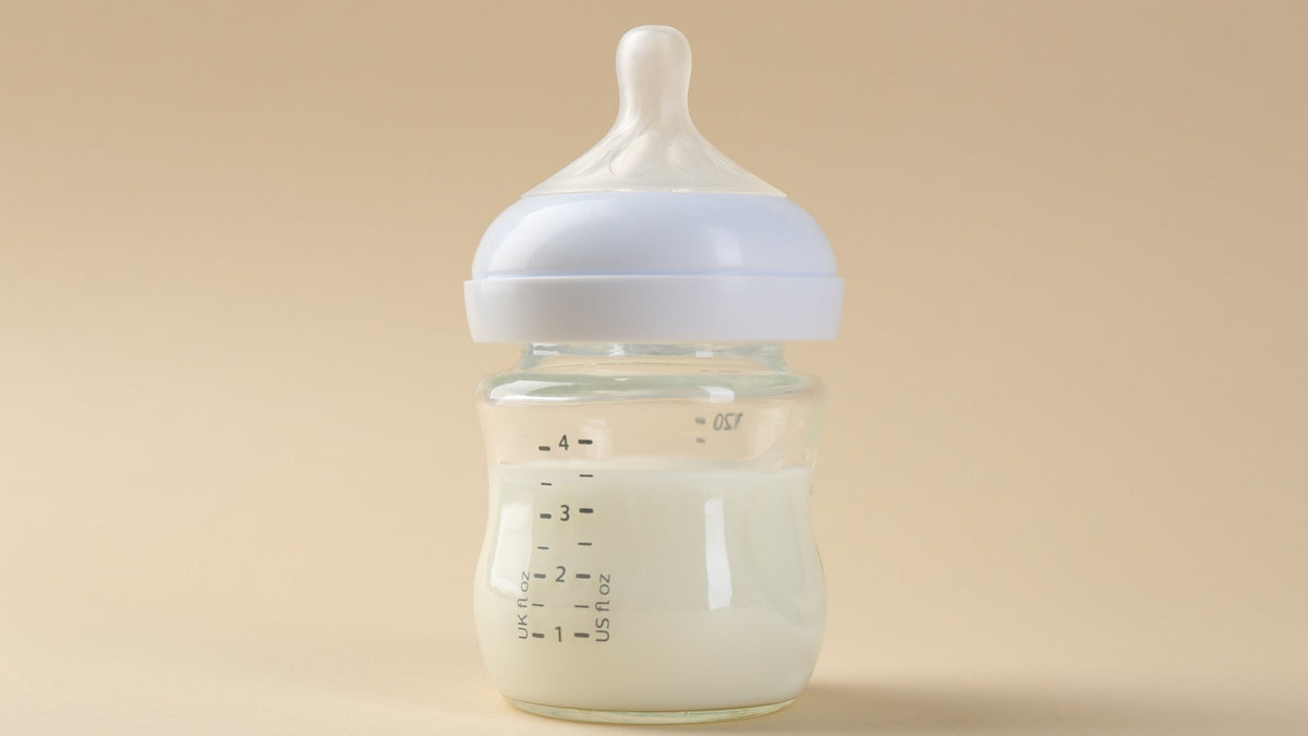 Several wet empty baby bottles and a bottle brush grouped on a white surface