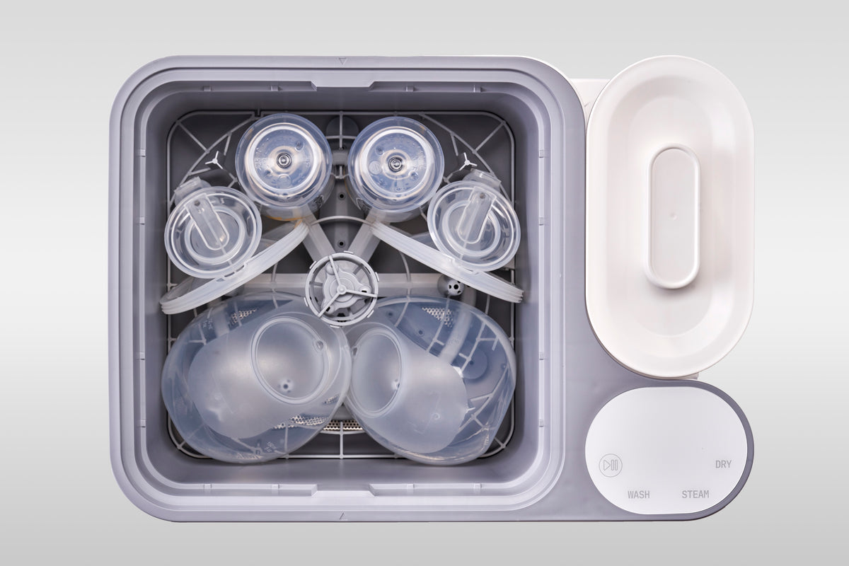 A wearable breast pump set and two bottles loaded together in the nuviebaby Clean Max washing basin, seen from above.