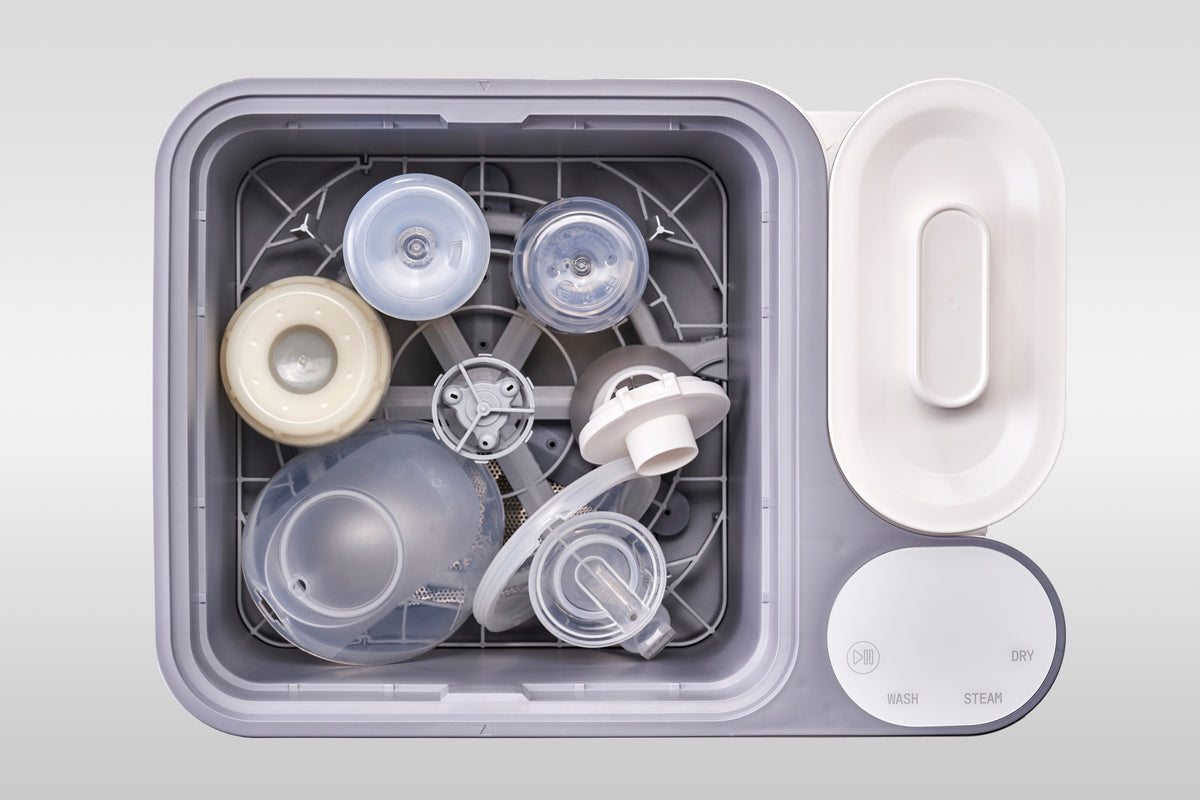 A mixed load of pump parts and bottles loaded together in the nuviebaby Clean Max washing basin, seen from above.